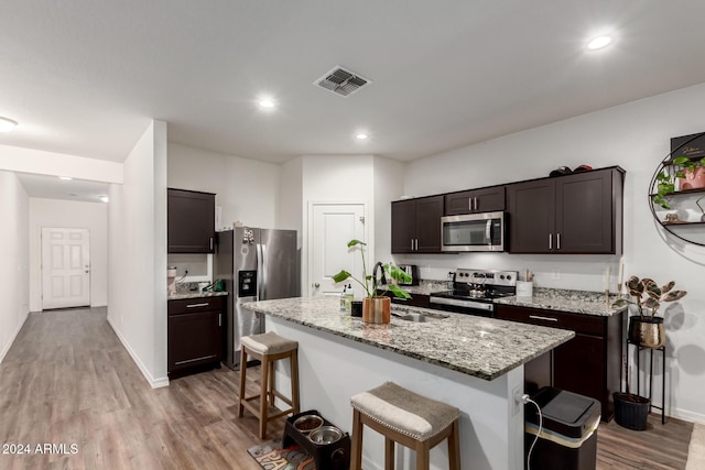 kitchen with appliances with stainless steel finishes, a kitchen breakfast bar, dark brown cabinets, a kitchen island with sink, and sink