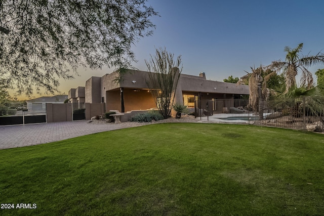 back house at dusk featuring a yard and a fenced in pool