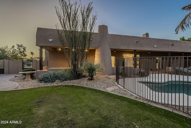 back house at dusk featuring a lawn, a patio, and a fenced in pool