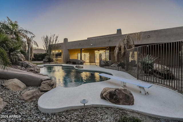 pool at dusk featuring a patio and a diving board