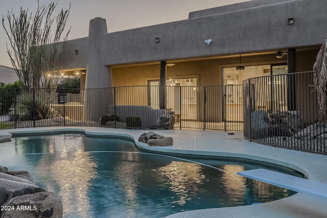 pool at dusk featuring a diving board and ceiling fan