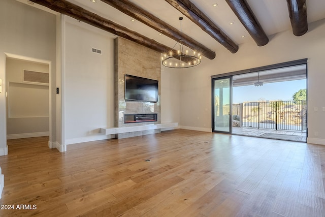 unfurnished living room featuring light wood-type flooring, a fireplace, beamed ceiling, and an inviting chandelier