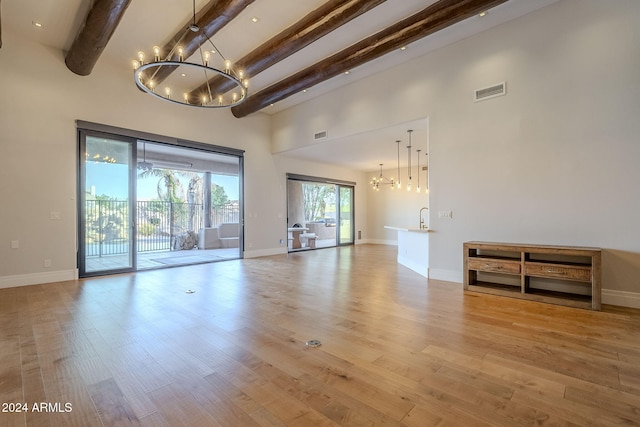 unfurnished living room featuring a high ceiling, light wood-type flooring, a chandelier, and beam ceiling