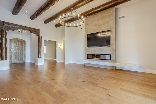 unfurnished living room featuring a high ceiling, light wood-type flooring, a tiled fireplace, and beamed ceiling