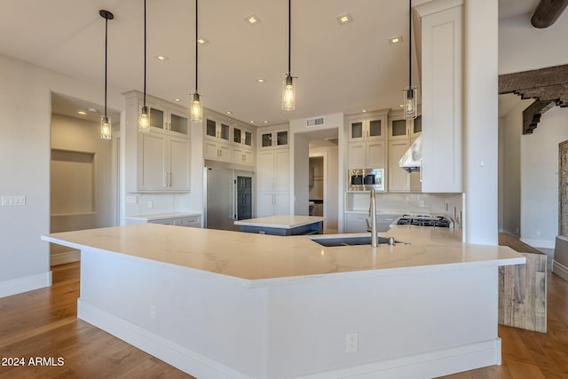 kitchen featuring built in appliances, white cabinetry, a large island with sink, hanging light fixtures, and ventilation hood