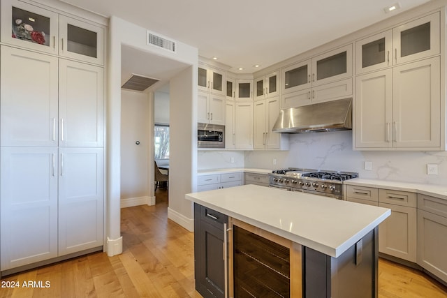 kitchen with a kitchen island, backsplash, appliances with stainless steel finishes, light hardwood / wood-style floors, and beverage cooler