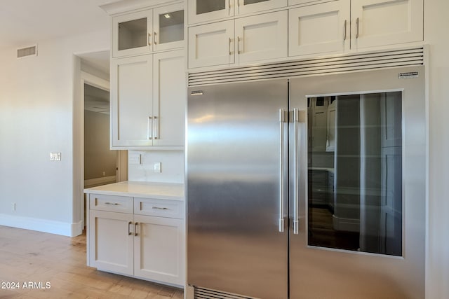 kitchen featuring built in fridge, light wood-type flooring, and white cabinets