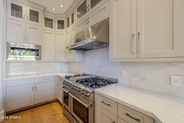 kitchen with light wood-type flooring, stainless steel appliances, tasteful backsplash, and light stone counters