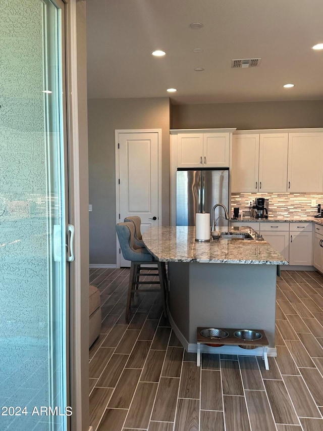 kitchen featuring sink, stainless steel fridge, white cabinets, and a kitchen island with sink