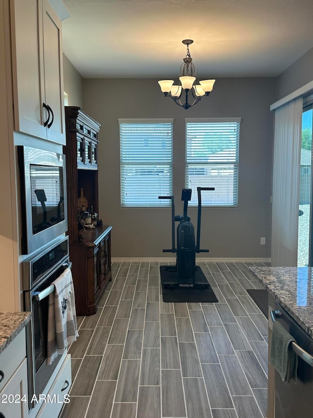 kitchen with decorative light fixtures, appliances with stainless steel finishes, light stone countertops, a chandelier, and dark wood-type flooring