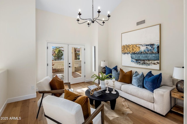 living room with a towering ceiling, a notable chandelier, light wood-type flooring, and french doors