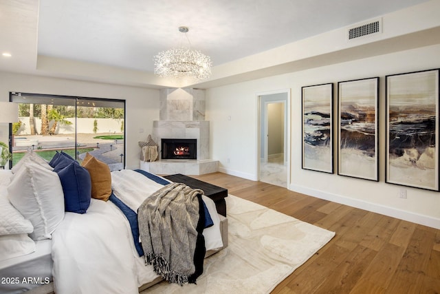 bedroom with wood-type flooring, access to outside, a notable chandelier, a raised ceiling, and a premium fireplace