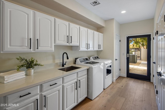 clothes washing area with separate washer and dryer, sink, light hardwood / wood-style floors, and cabinets