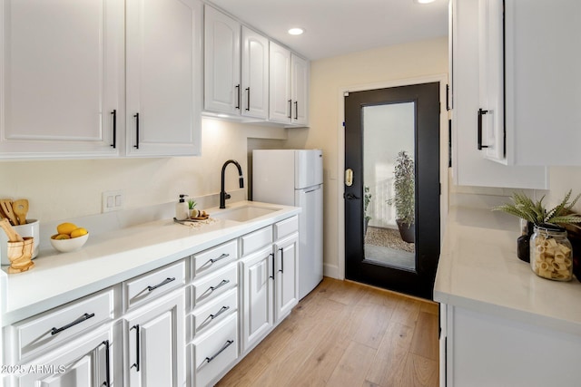 kitchen with light wood-type flooring, sink, white fridge, and white cabinets