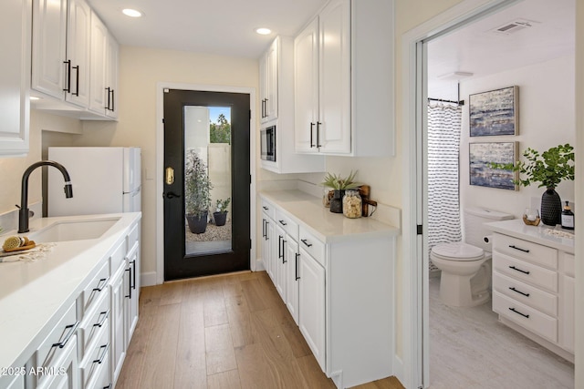 kitchen featuring white cabinetry, sink, white refrigerator, and light wood-type flooring