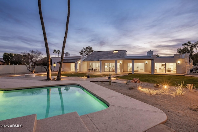 pool at dusk with a patio and a lawn