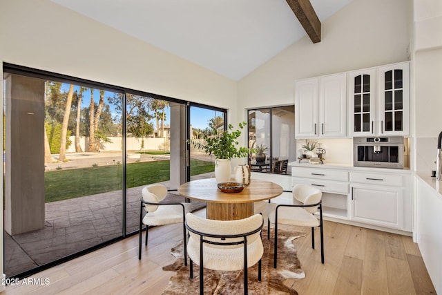 dining space with high vaulted ceiling, beam ceiling, and light hardwood / wood-style flooring