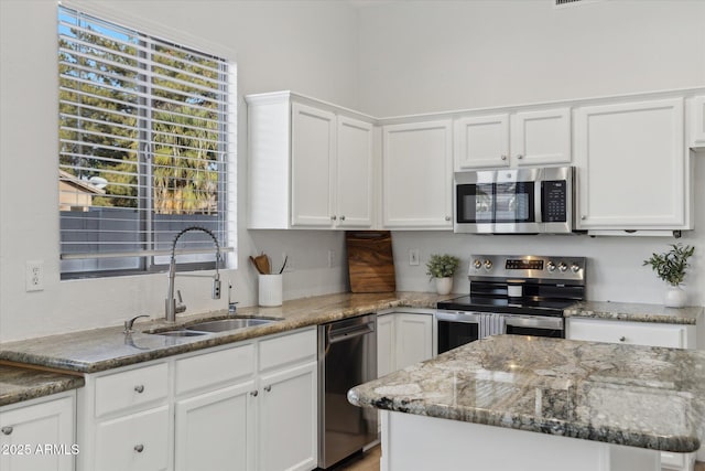 kitchen featuring stone counters, a sink, white cabinets, appliances with stainless steel finishes, and a center island