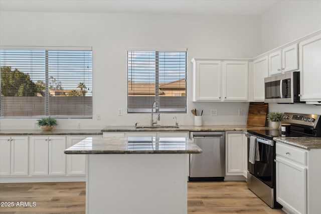 kitchen featuring stone counters, appliances with stainless steel finishes, white cabinetry, a sink, and a kitchen island