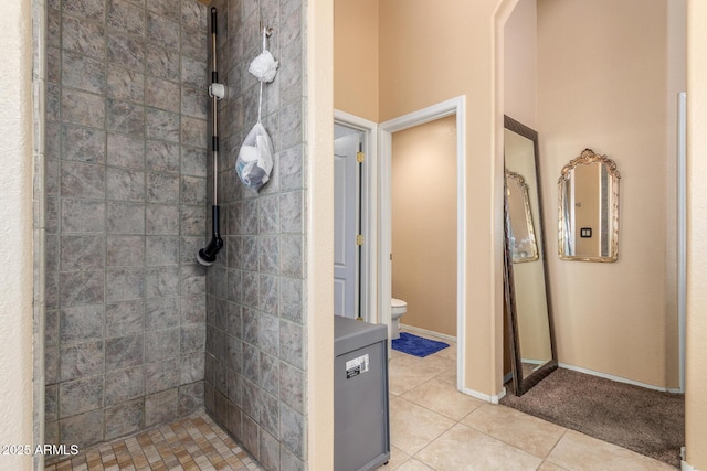 full bathroom with tile patterned flooring, baseboards, a tile shower, and toilet