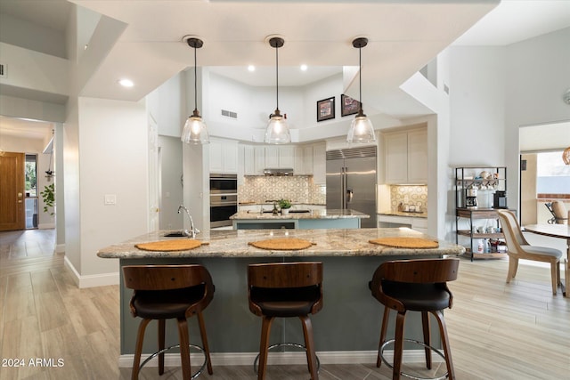 kitchen featuring light stone countertops, tasteful backsplash, stainless steel built in fridge, a high ceiling, and hanging light fixtures