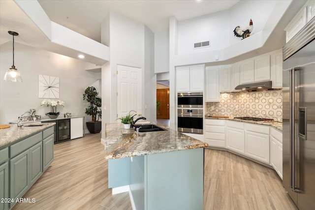 kitchen with white cabinetry, a towering ceiling, an island with sink, and appliances with stainless steel finishes