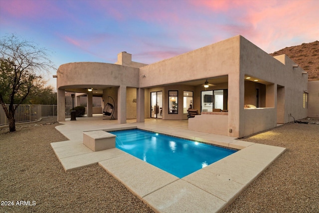 pool at dusk featuring ceiling fan and a patio area