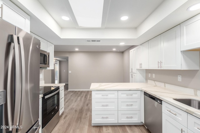 kitchen with light stone counters, kitchen peninsula, white cabinetry, light wood-type flooring, and appliances with stainless steel finishes