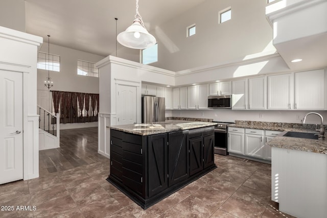 kitchen with stainless steel appliances, a high ceiling, a sink, a kitchen island, and dark cabinets