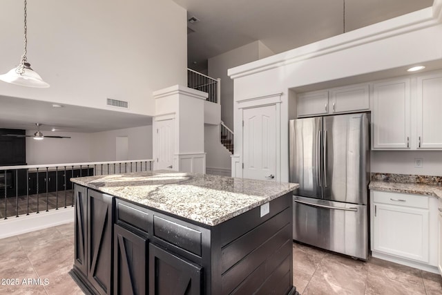 kitchen featuring visible vents, ceiling fan, a kitchen island, light stone counters, and freestanding refrigerator