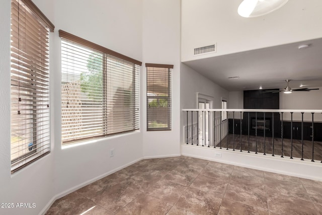 unfurnished room with visible vents, ceiling fan, a towering ceiling, and baseboards