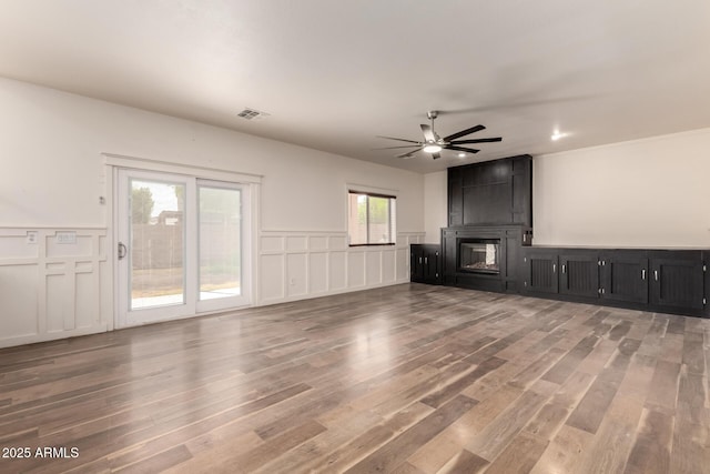 unfurnished living room with a fireplace, visible vents, a decorative wall, ceiling fan, and wood finished floors