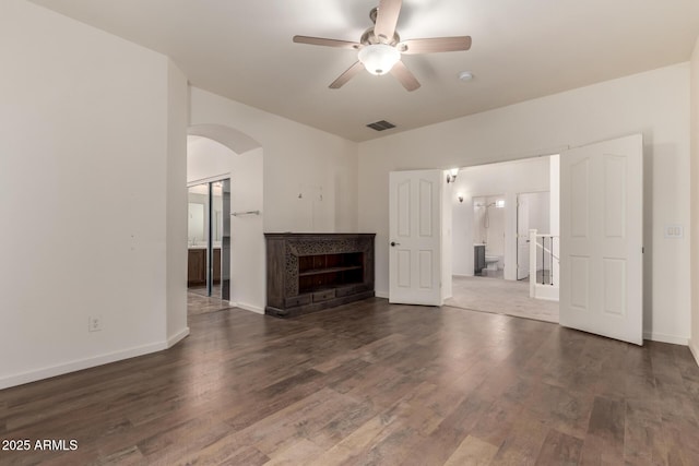 unfurnished living room featuring baseboards, visible vents, arched walkways, dark wood-type flooring, and a fireplace