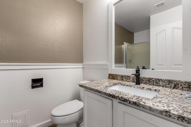 full bath with a shower with door, visible vents, a textured wall, toilet, and vanity