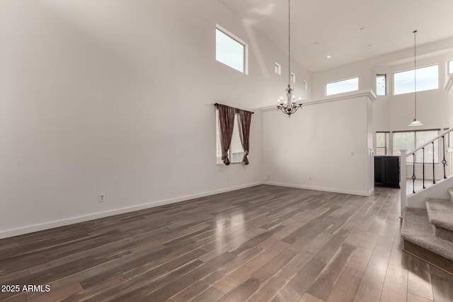 unfurnished living room featuring dark wood-style flooring, a notable chandelier, a high ceiling, baseboards, and stairs