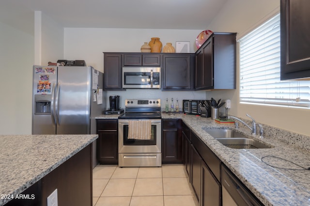 kitchen with dark brown cabinets, sink, light stone countertops, appliances with stainless steel finishes, and light tile patterned floors