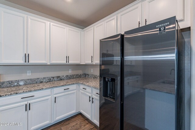 kitchen with dark hardwood / wood-style flooring, black fridge, and white cabinets