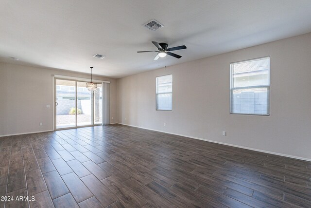 spare room with ceiling fan with notable chandelier, dark wood-type flooring, and a wealth of natural light