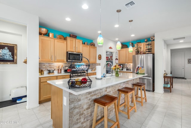 kitchen with appliances with stainless steel finishes, light brown cabinetry, a breakfast bar, a center island with sink, and hanging light fixtures