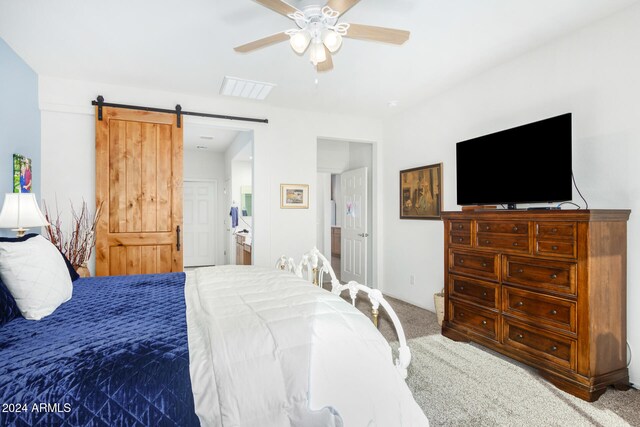 carpeted bedroom with a barn door, ceiling fan, and ensuite bath