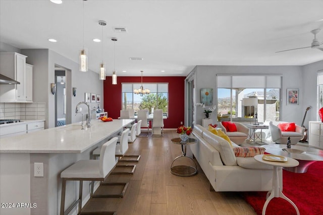 living room featuring light wood-type flooring, sink, ceiling fan with notable chandelier, and plenty of natural light