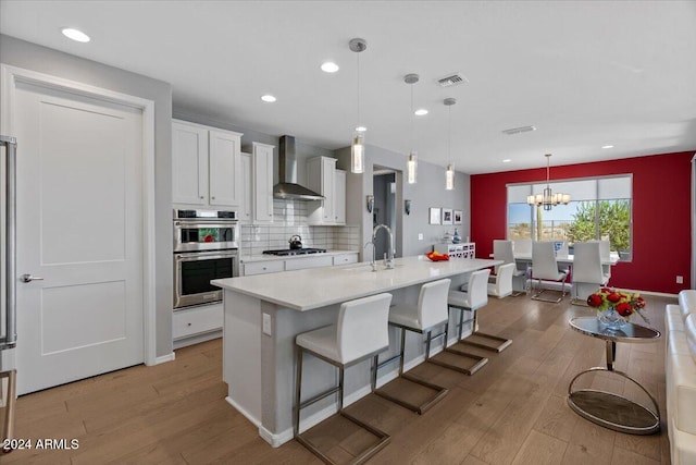 kitchen featuring light hardwood / wood-style floors, wall chimney exhaust hood, white cabinetry, and pendant lighting