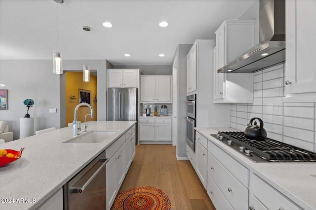 kitchen featuring white cabinets, wall chimney exhaust hood, sink, light wood-type flooring, and appliances with stainless steel finishes