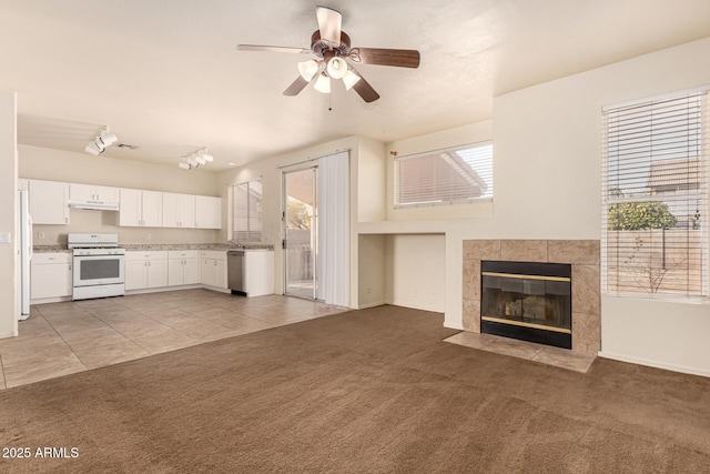 unfurnished living room featuring light colored carpet, ceiling fan, and a tiled fireplace