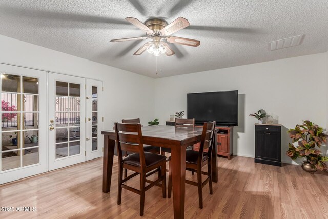 dining area featuring visible vents, french doors, light wood-style floors, a textured ceiling, and a ceiling fan