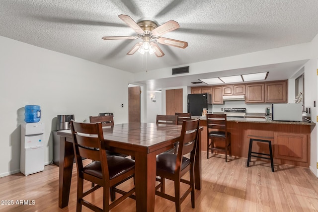 dining room featuring visible vents, a textured ceiling, ceiling fan, and light wood finished floors