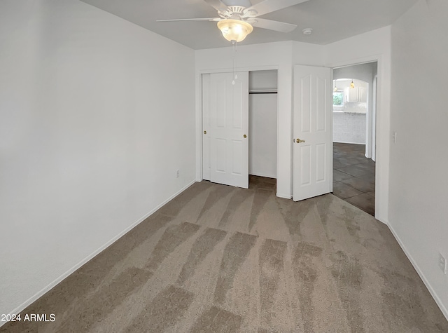 unfurnished bedroom with dark carpet, ceiling fan, and a closet