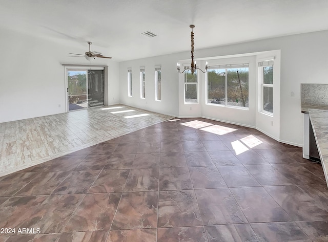 unfurnished living room with ceiling fan with notable chandelier, dark wood-type flooring, and plenty of natural light