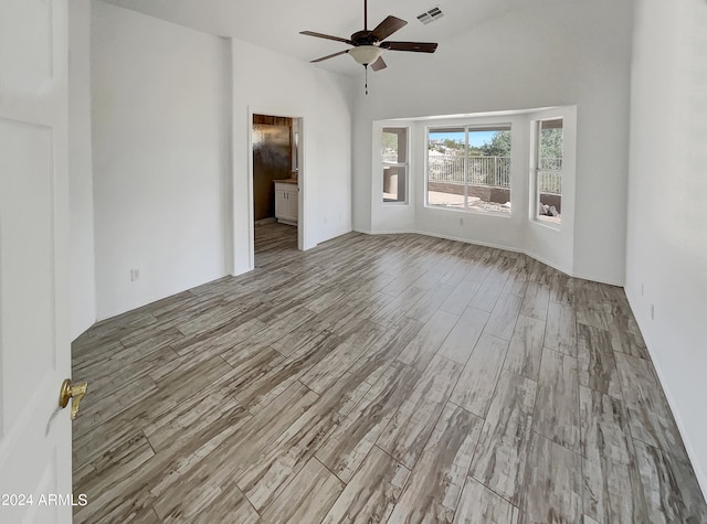 unfurnished living room featuring ceiling fan, light wood-type flooring, and a high ceiling