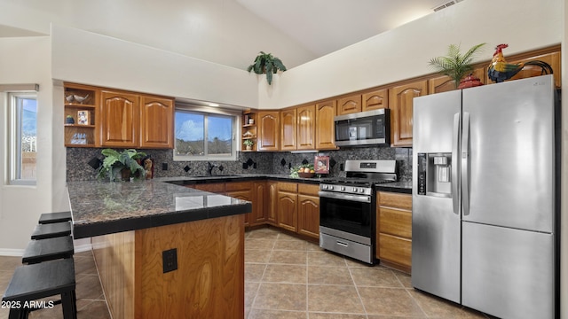 kitchen featuring appliances with stainless steel finishes, tasteful backsplash, lofted ceiling, light tile patterned floors, and kitchen peninsula